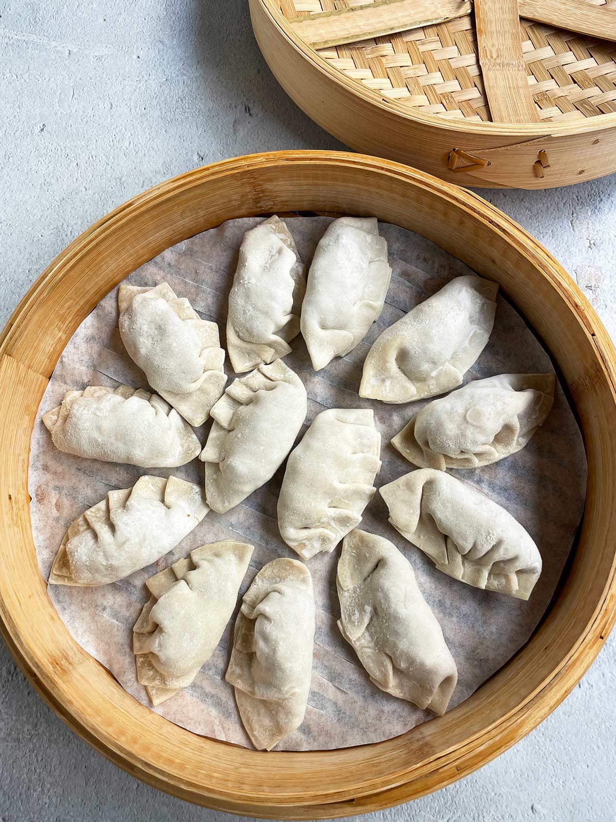 Frozen mandu on parchment paper in a bamboo steamer basket