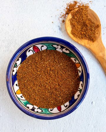 Blue bowl of baharat with a wooden spoon.