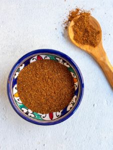 Baharat spice mix in a blue bowl with wooden spoon on the side.