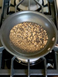 Whole baharat spices in a small frying pan.