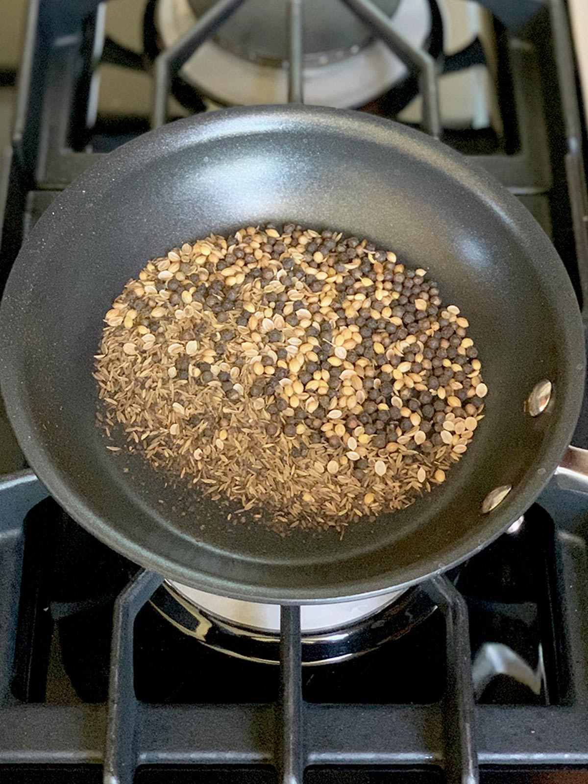 Whole spices in frying pan heating up on stove top.