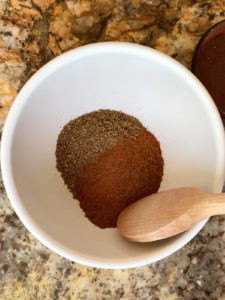 Spices in a white bowl with a wooden spoon ready to be mixed together.