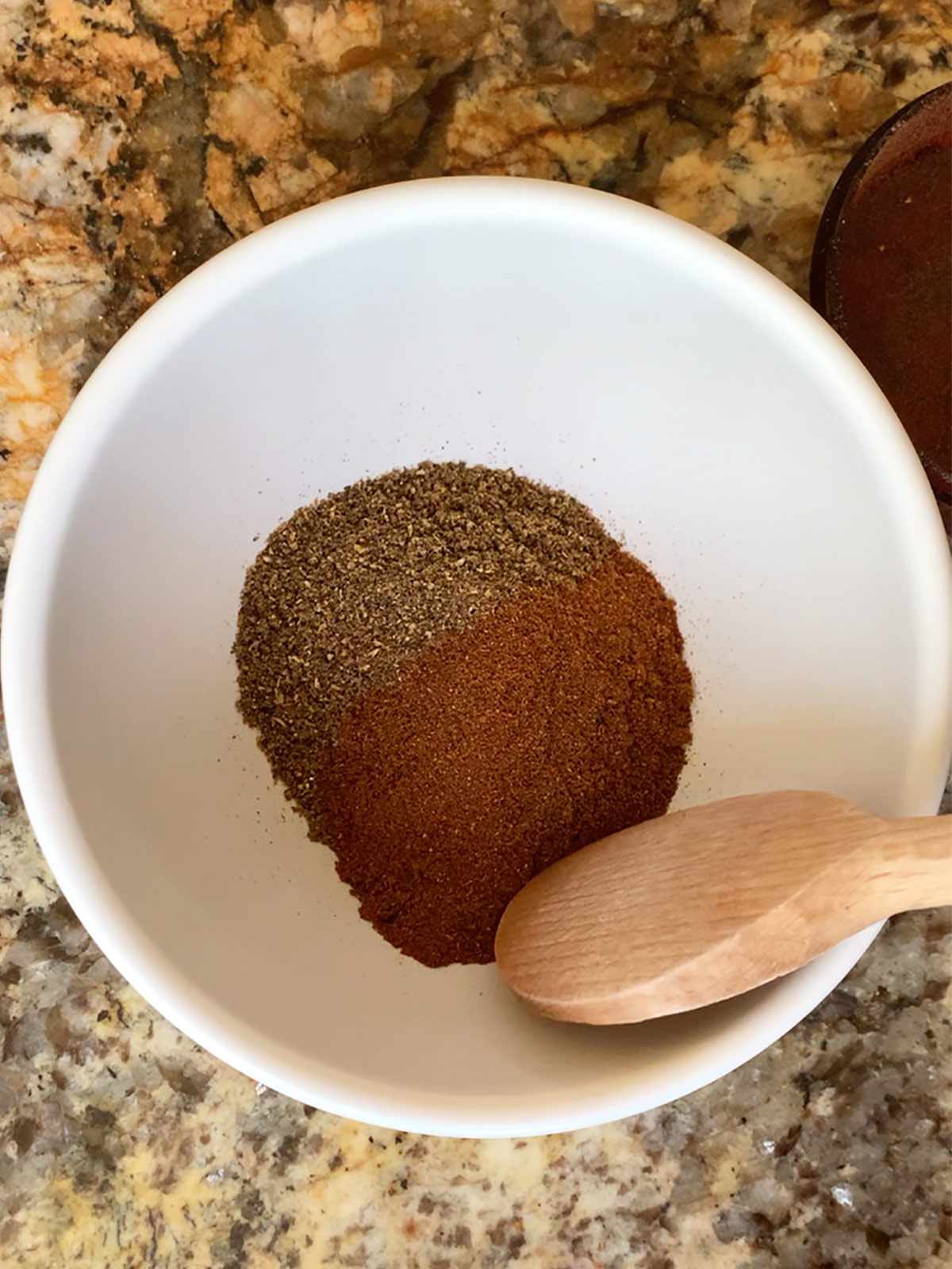 Baharat spices in bowl with wooden spoon ready to be mixed.