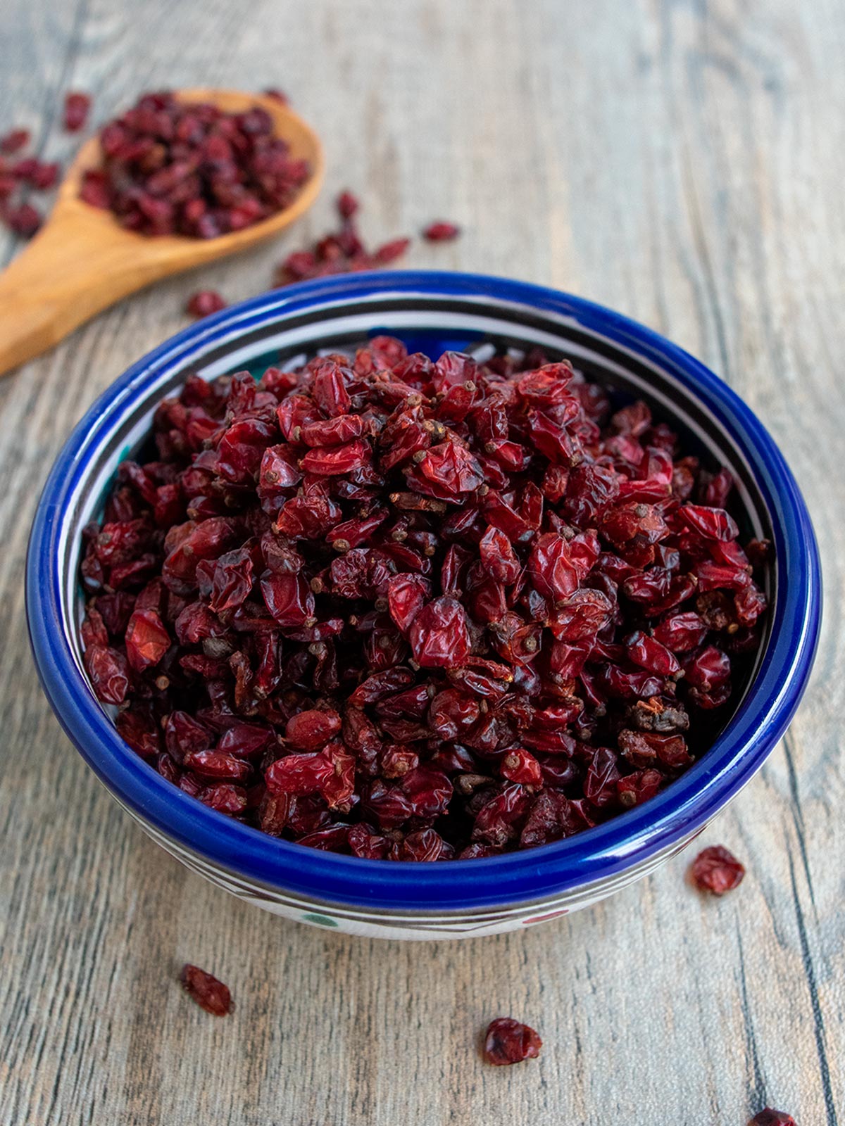 Blue bowl of barberries with a wooden spoon in the background.