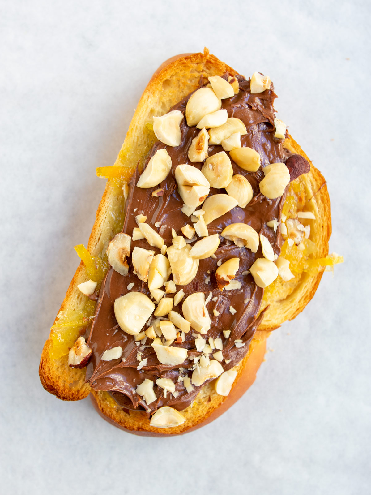 Close up of nutella tartine with orange marmalade and nutella and hazelnuts on challah toast.
