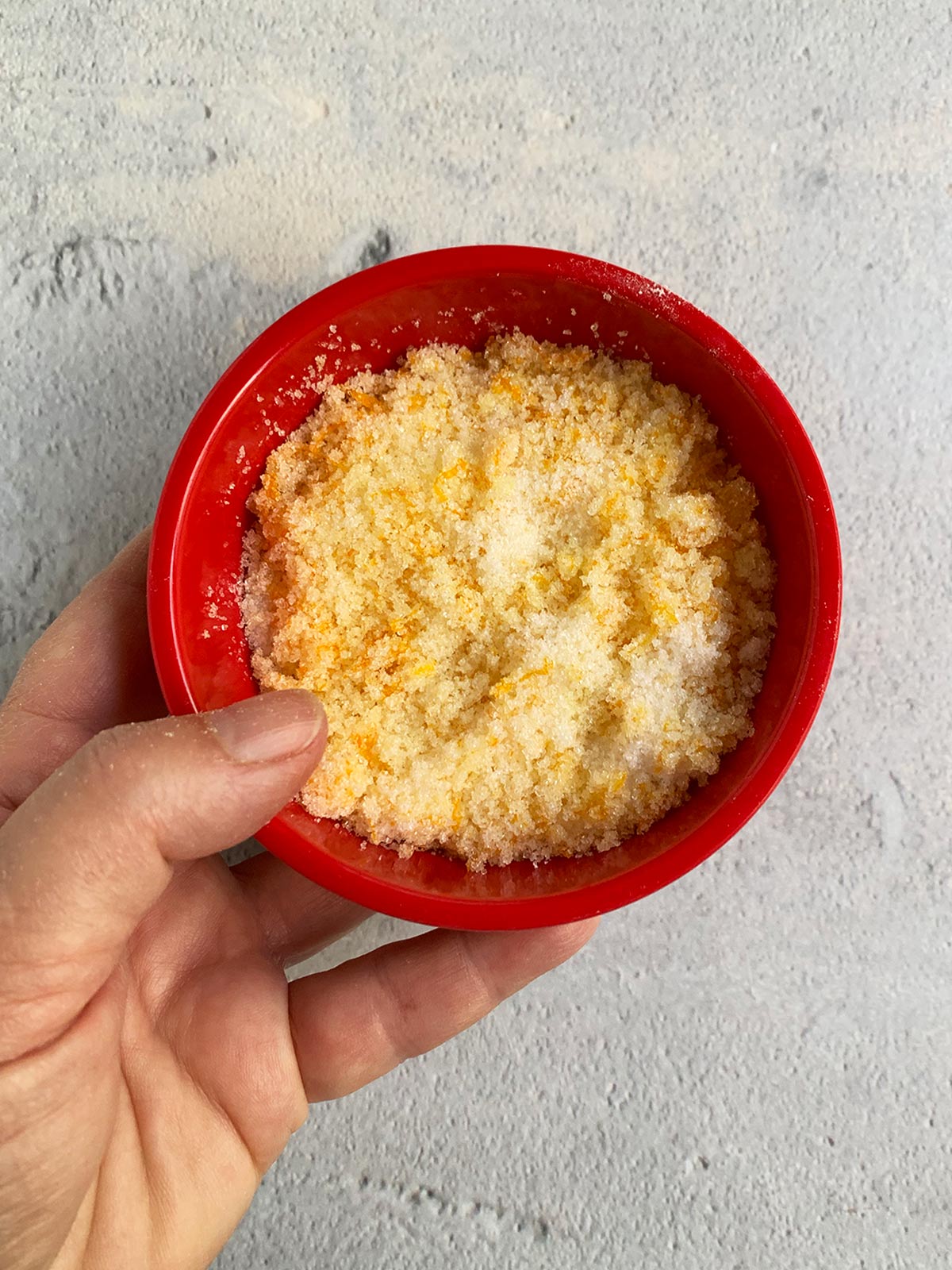 Orange zest and sugar mixed together in a red bowl.