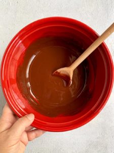 Melted butter and chocolate shiny and mixed in a red bowl with wooden spoon.