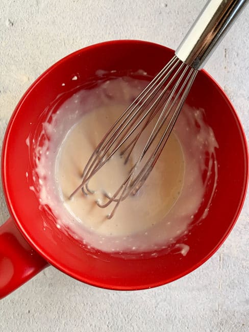 Cream cheese glaze in a red bowl with a whisk.