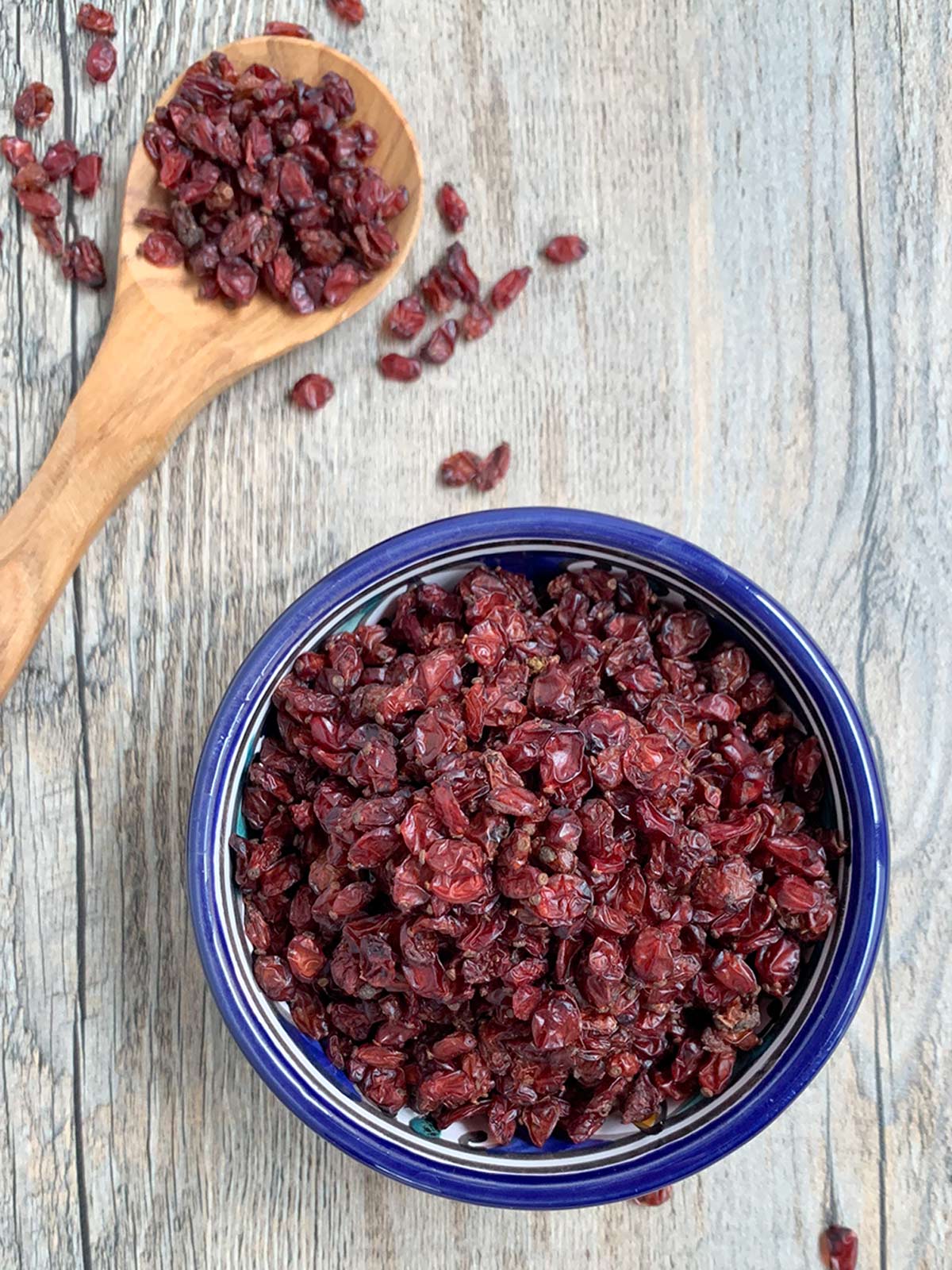 Barberries straight down offset in blue bowl w wooden spoon.