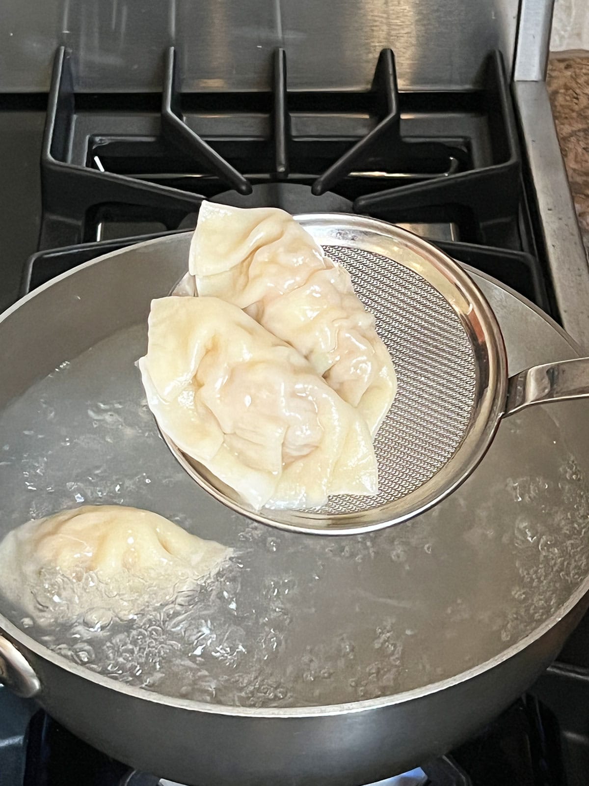 Boiled mandu with 2 on a strainer over the boiling pot of water.