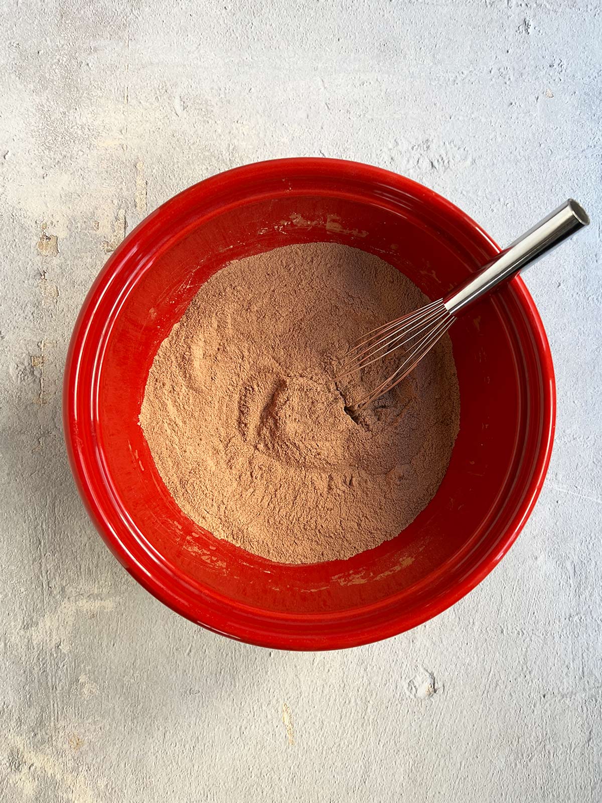 Dry ingredients for chocolate cake in a red bowl with a whisk.