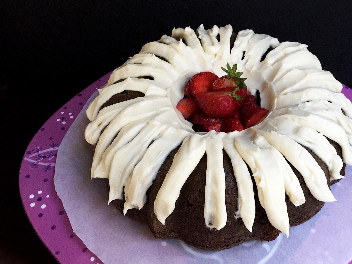 Chocolate cake with cream cheese frosting applied in stripes with fresh strawberries in the center on a purple cake stand.