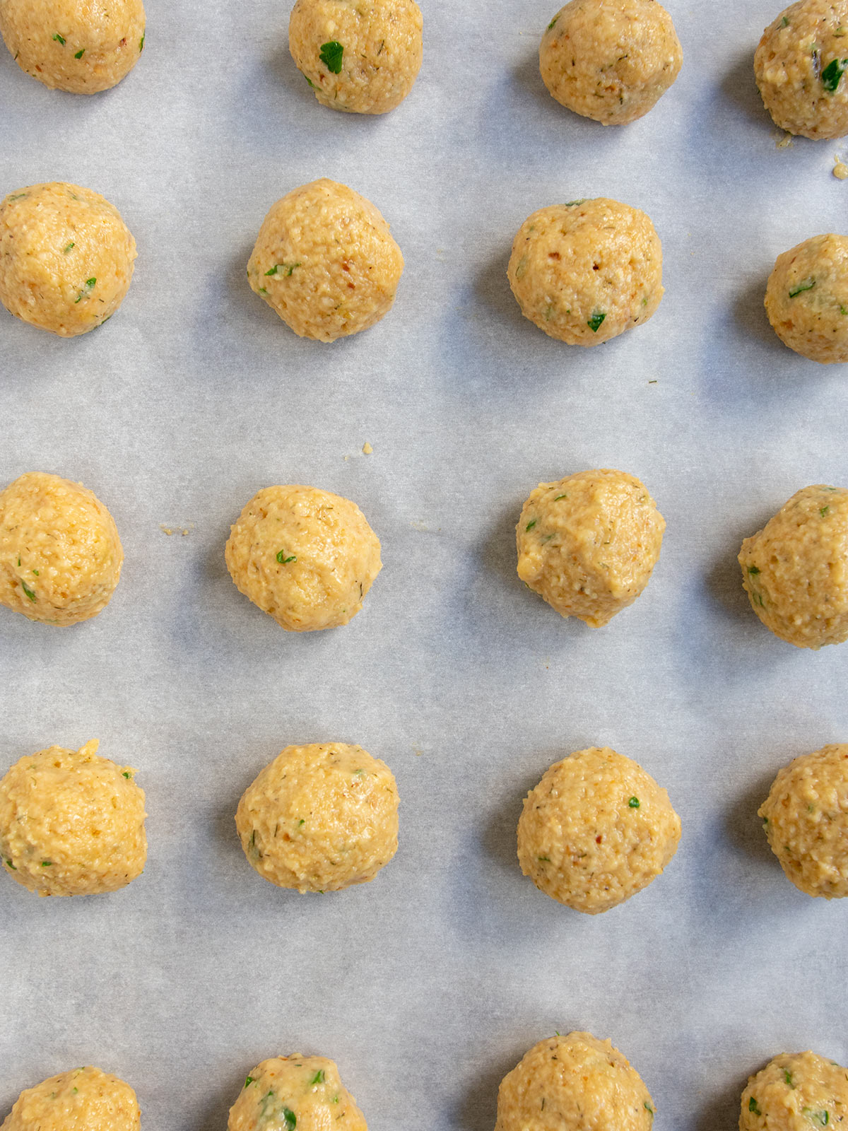 Matzo balls uncooked on white parchment paper.