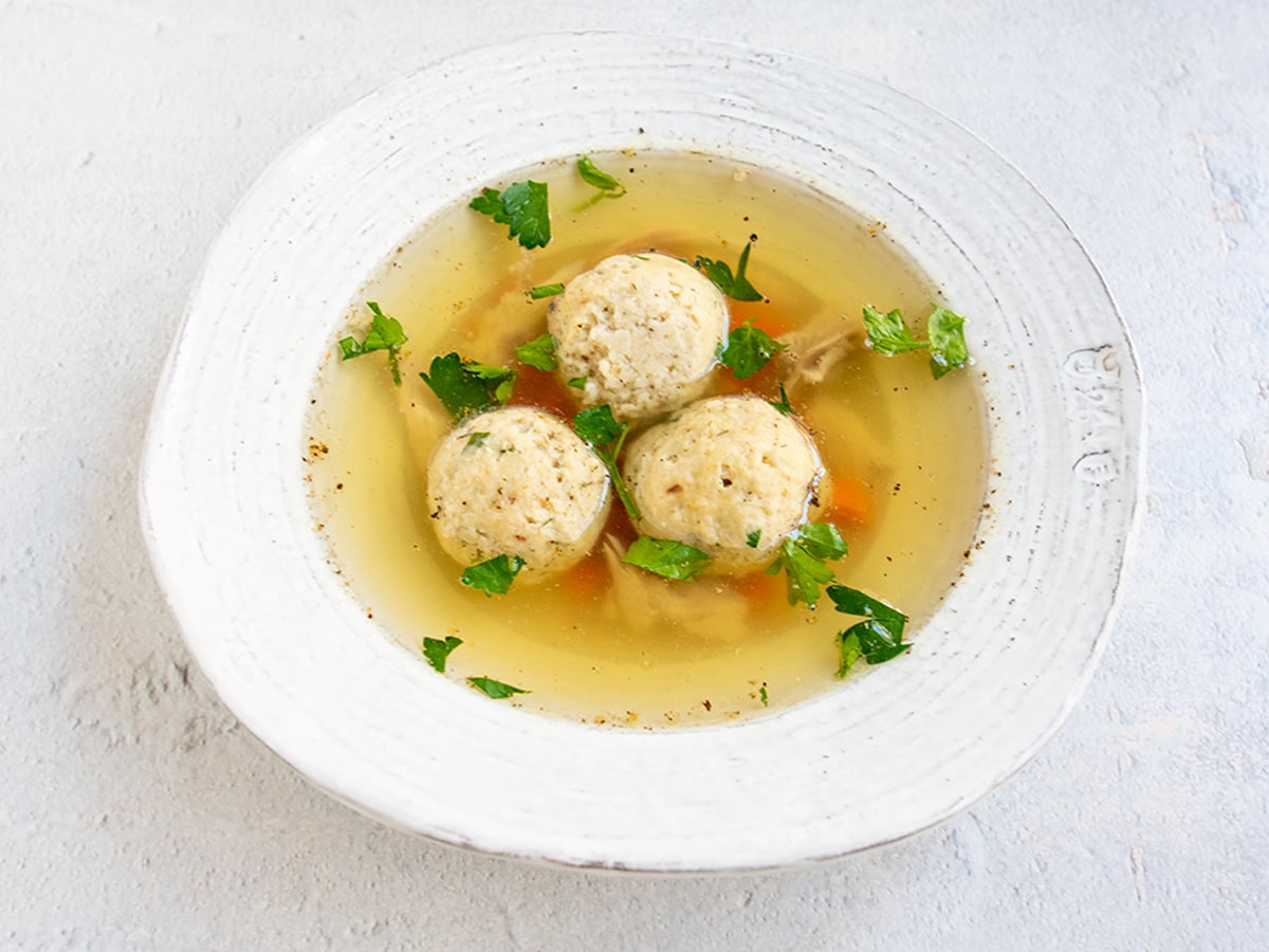 Matzo ball soup in a white bowl with herbs on top.