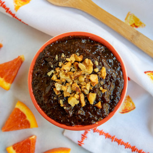 Lekvar in an orange bowl with oranges and an wooden spoon.
