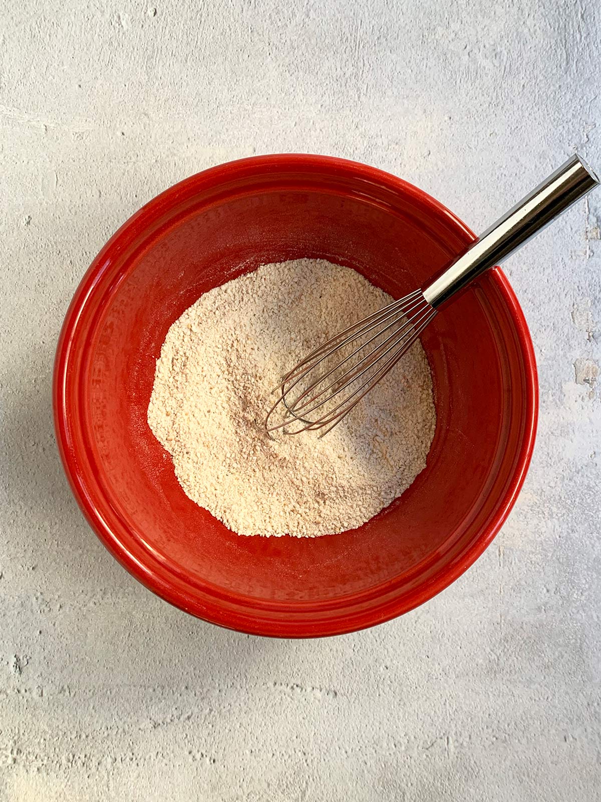 Dry matzo ball ingredients in a red bowl with a small whisk.