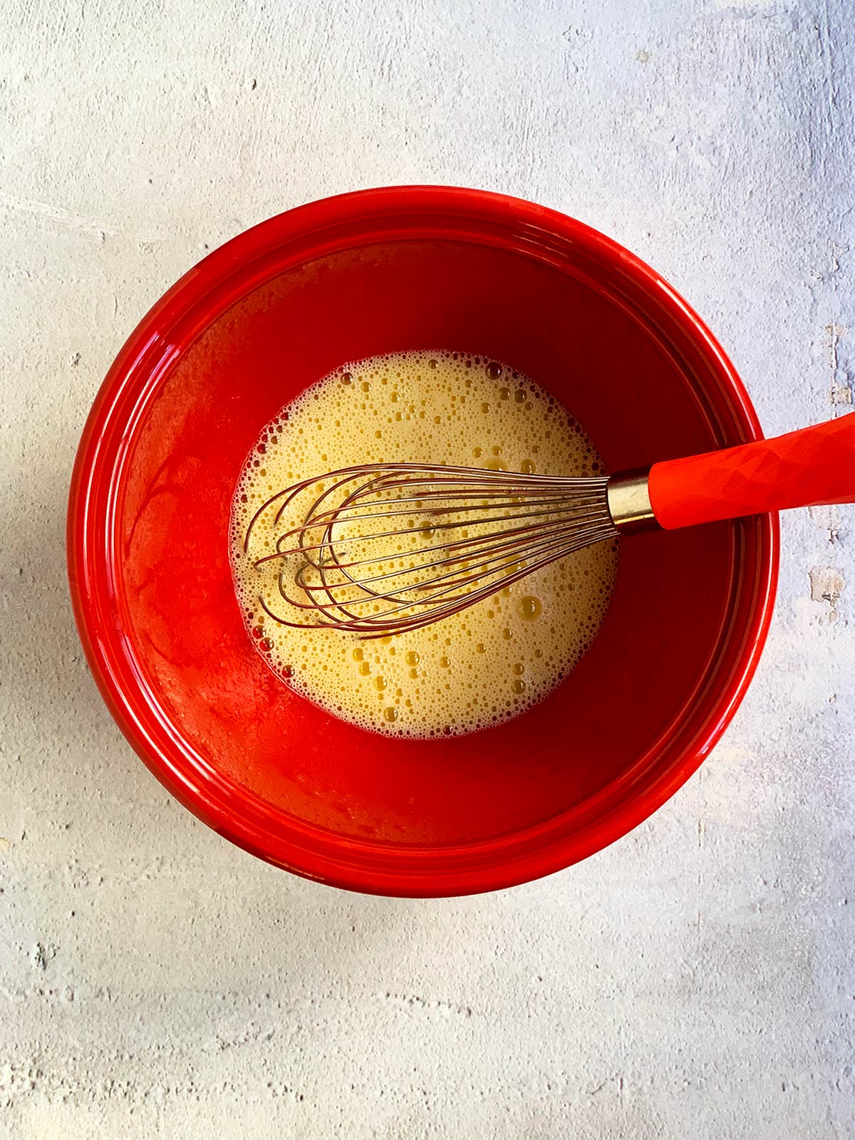 Matzo ball wet ingredients in a red bowl with a larger whisk.