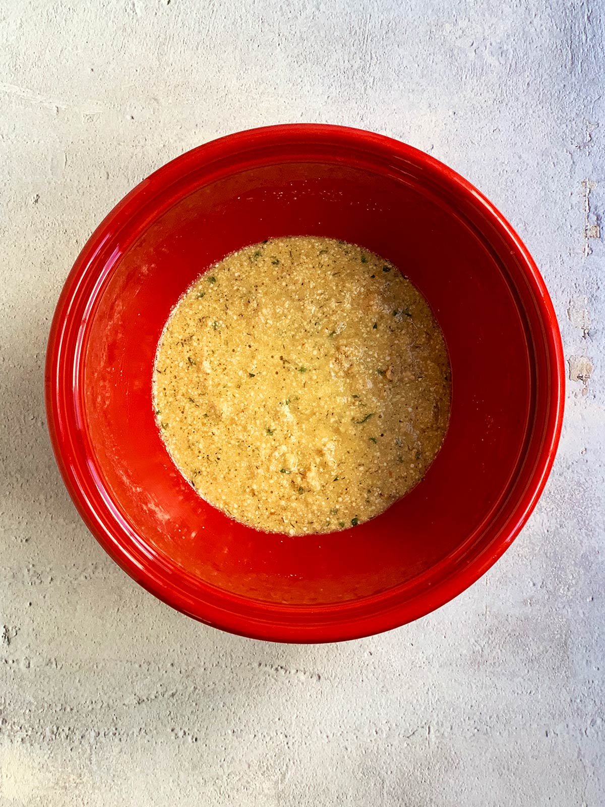 Matzo ball batter mixed ina red bowl ready to refrigerate.