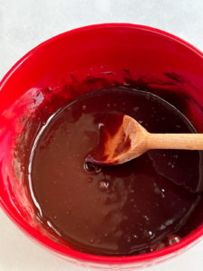 Wooden spoon mixing chocolate in a red bowl.