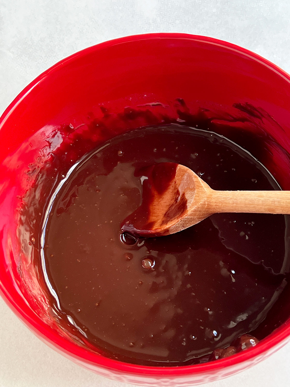 Chocolate truffle mixture with wooden spoon in red bowl.