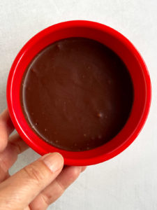 Refrigerated dairy-free chocolate truffle mixture in red bowl with hand.