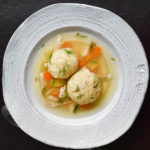 Matzo ball soup in a white bowl on a black background.