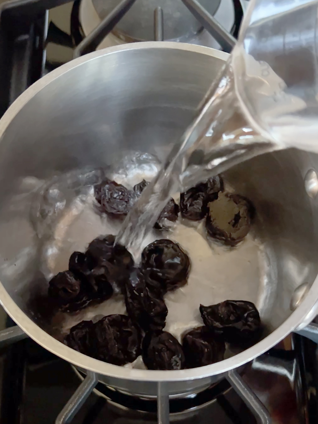 Prunes in pot with water being poured over them.
