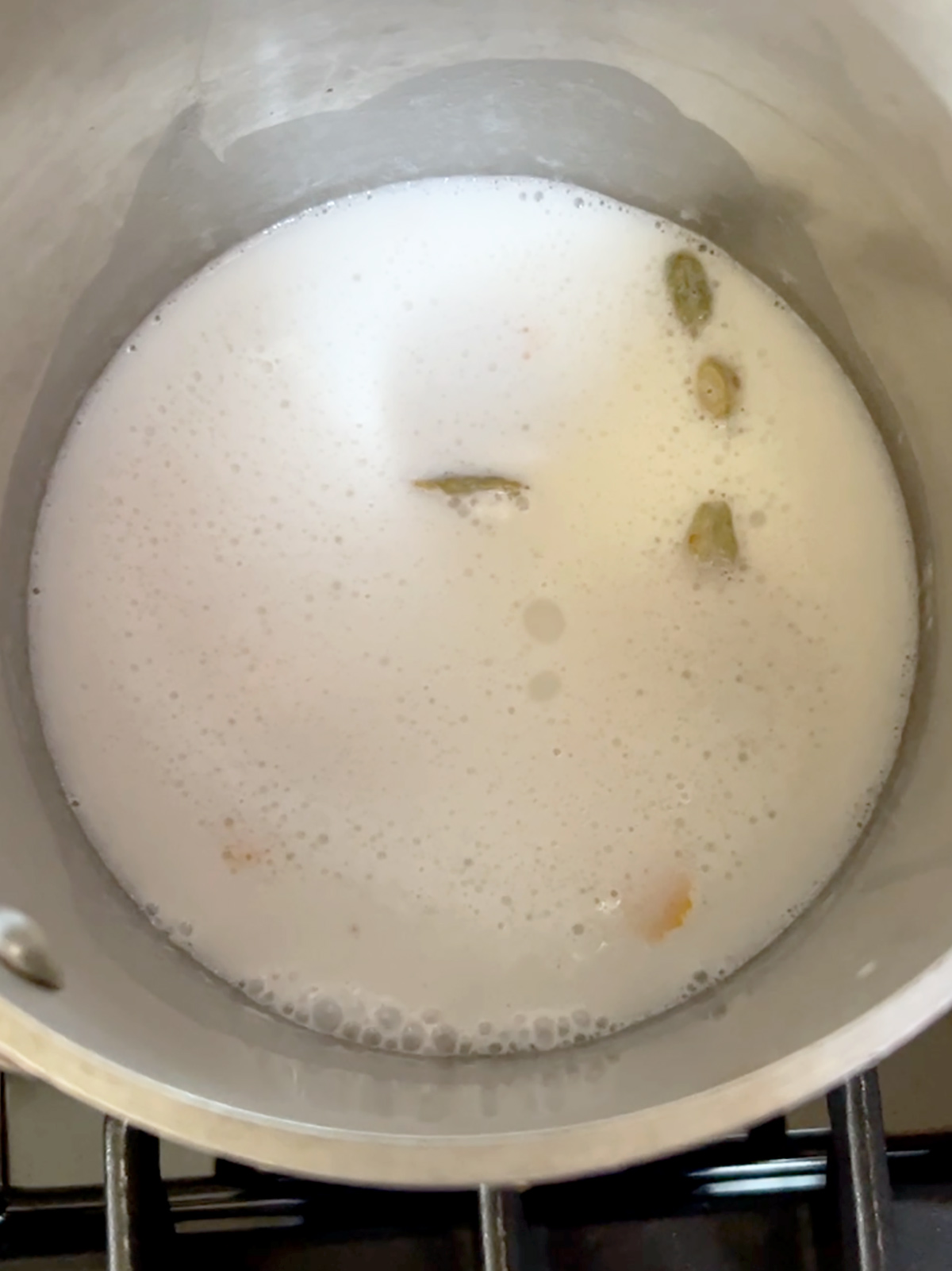 Coconut cream and cardamom and orange zest boiling in a small pot.