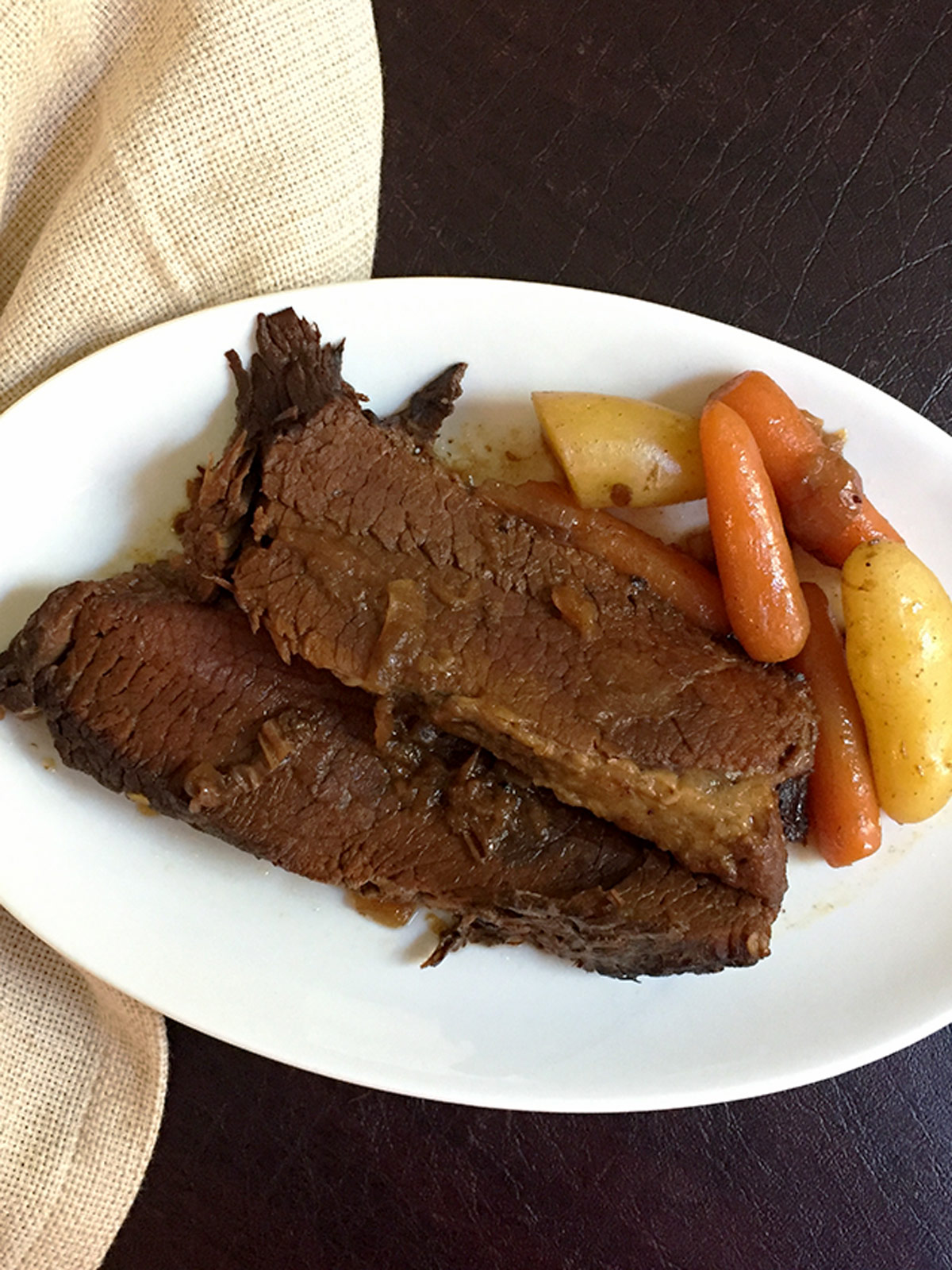 Two slices of instant pot brisket on a white plate with carrots and potatoes.
