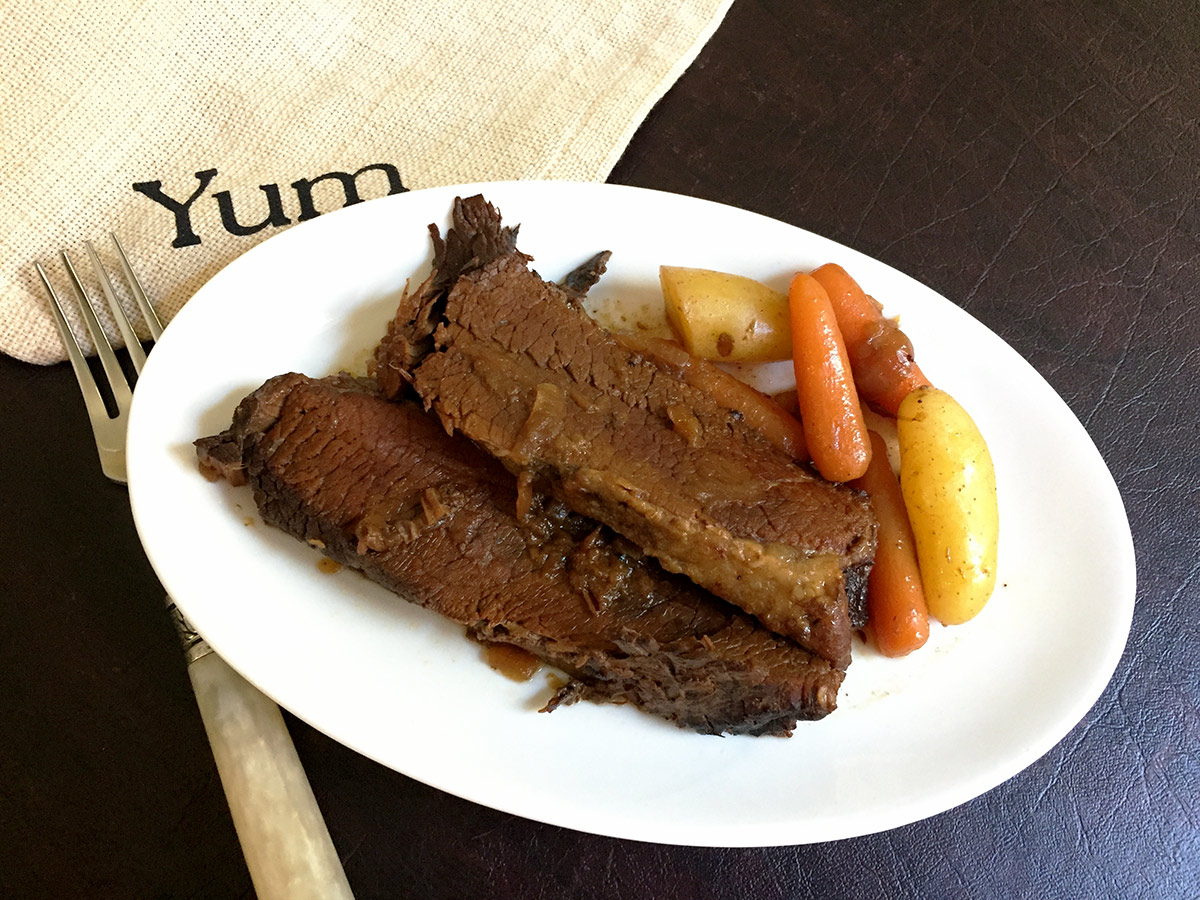 Instant pot brisket on a white plate with a fork and a napkin.