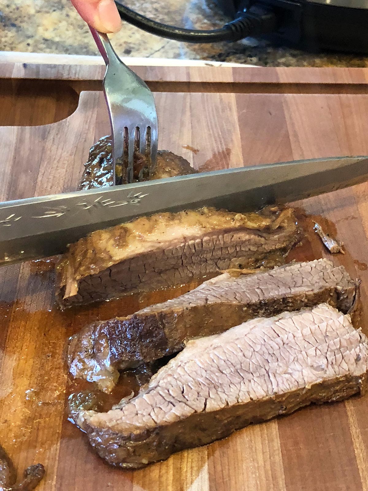 Person slicing brisket on a wooden cutting board.