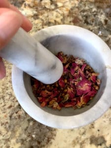 Dried spices plus rose petals in mortar and pestle.