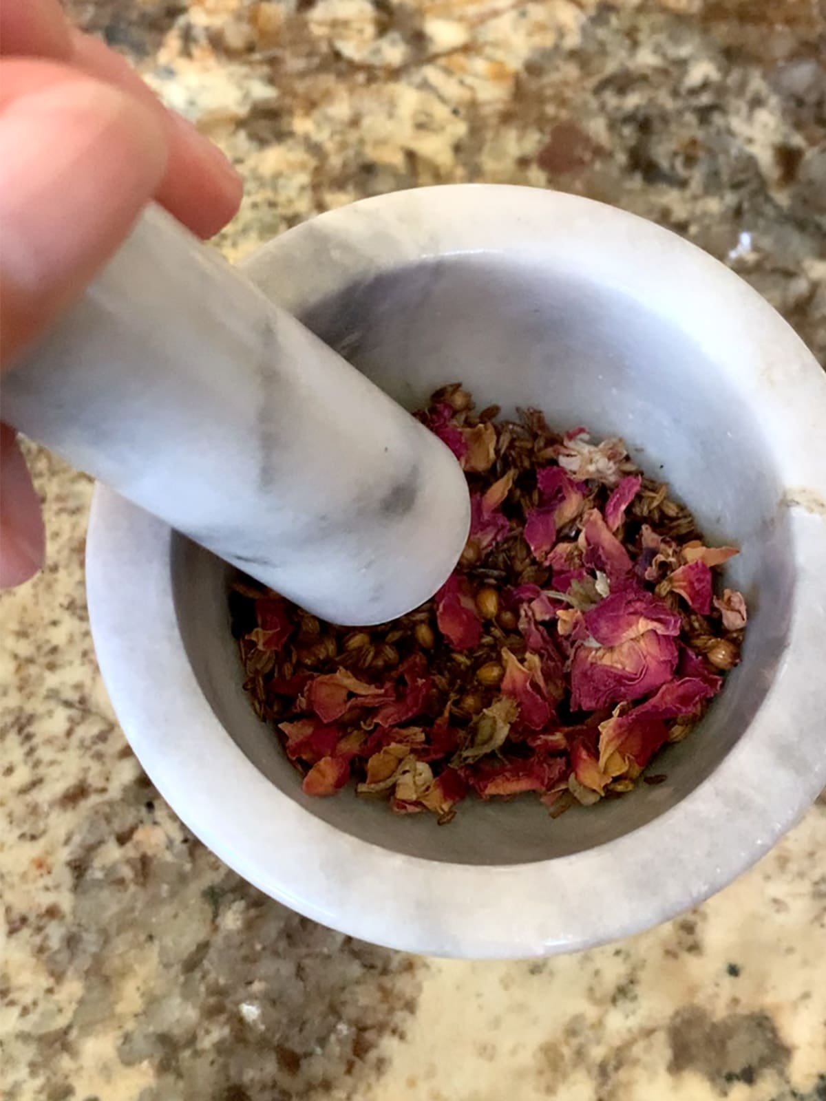 Spices and rose petals in mortar and pestle.