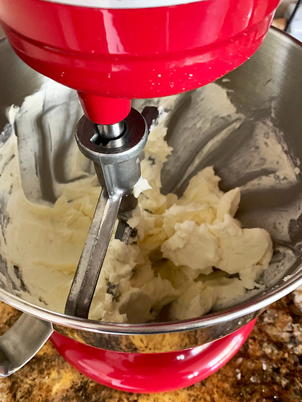 Cream cheese and sugar being combined in a red stand mixer with paddle attachment.