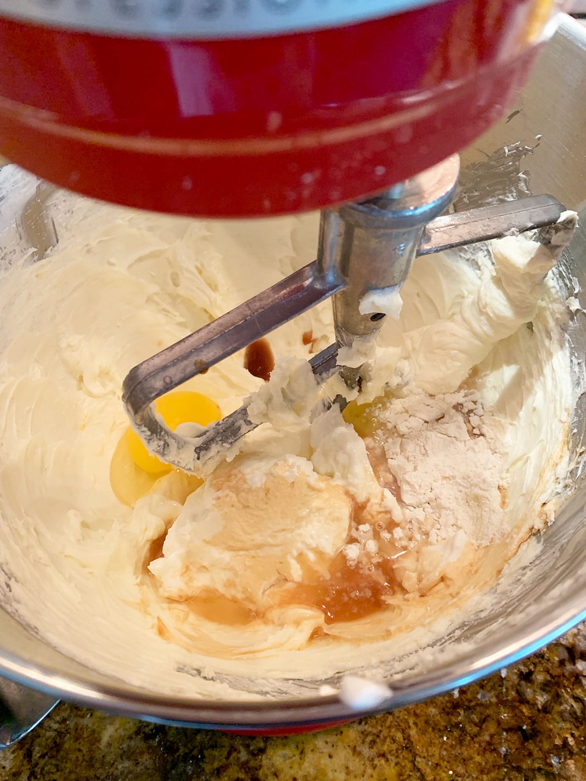 Cheesecake filling with all ingredients added being mixed with paddle attachment in a red stand mixer.