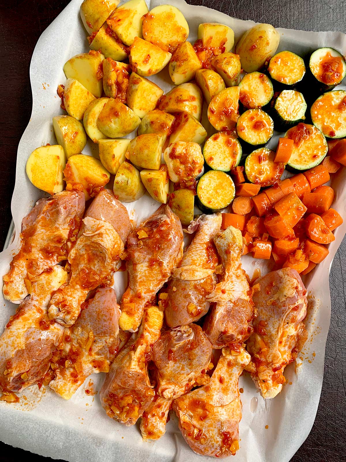 Tray of chicken legs and carrots, potatoes and zucchini with harissa sauce.