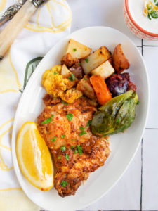 Harissa chicken and vegetables on a white plate with a slice of lemon.