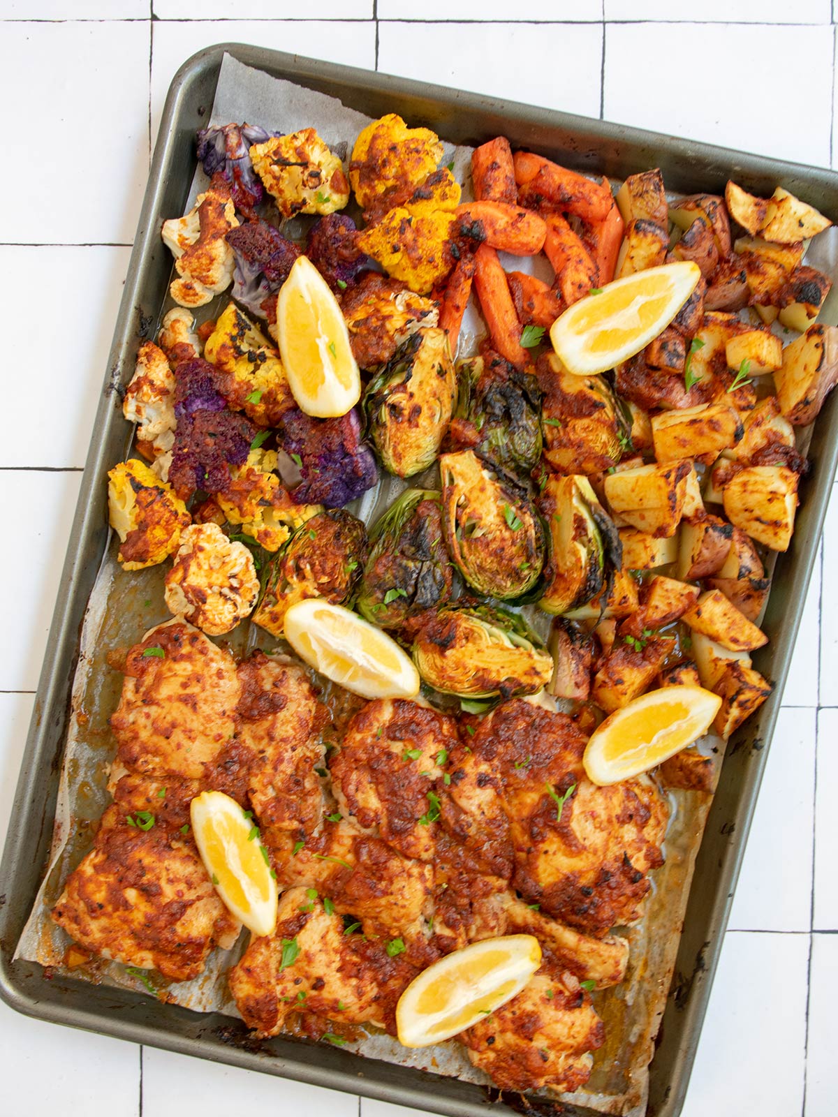 Harissa chicken and vegetables cooked on sheet tray with lemon slices on top.