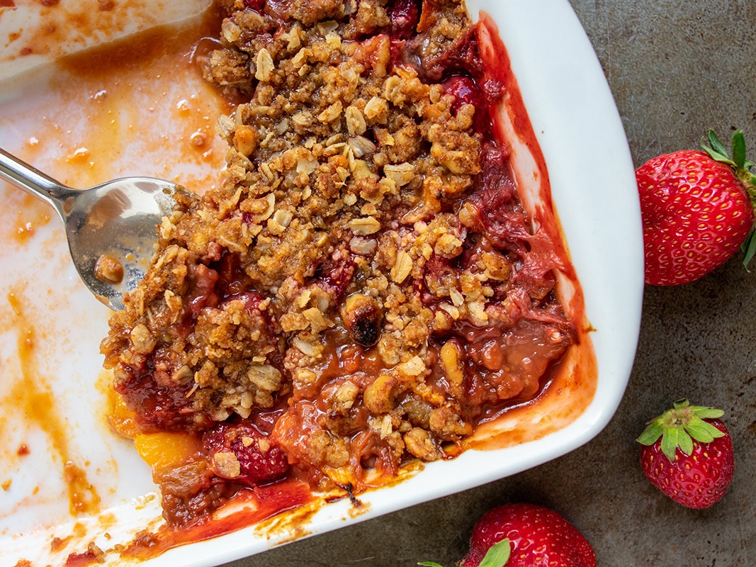 Fruit crisp baked in a white rectangular pan with serving spoon scooping some out.
