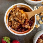 Cooked fruit crisp in a round white ramekin with a wooden spoon.