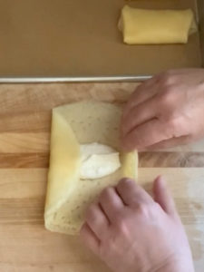 Folding a cheese blintz on a wooden board.