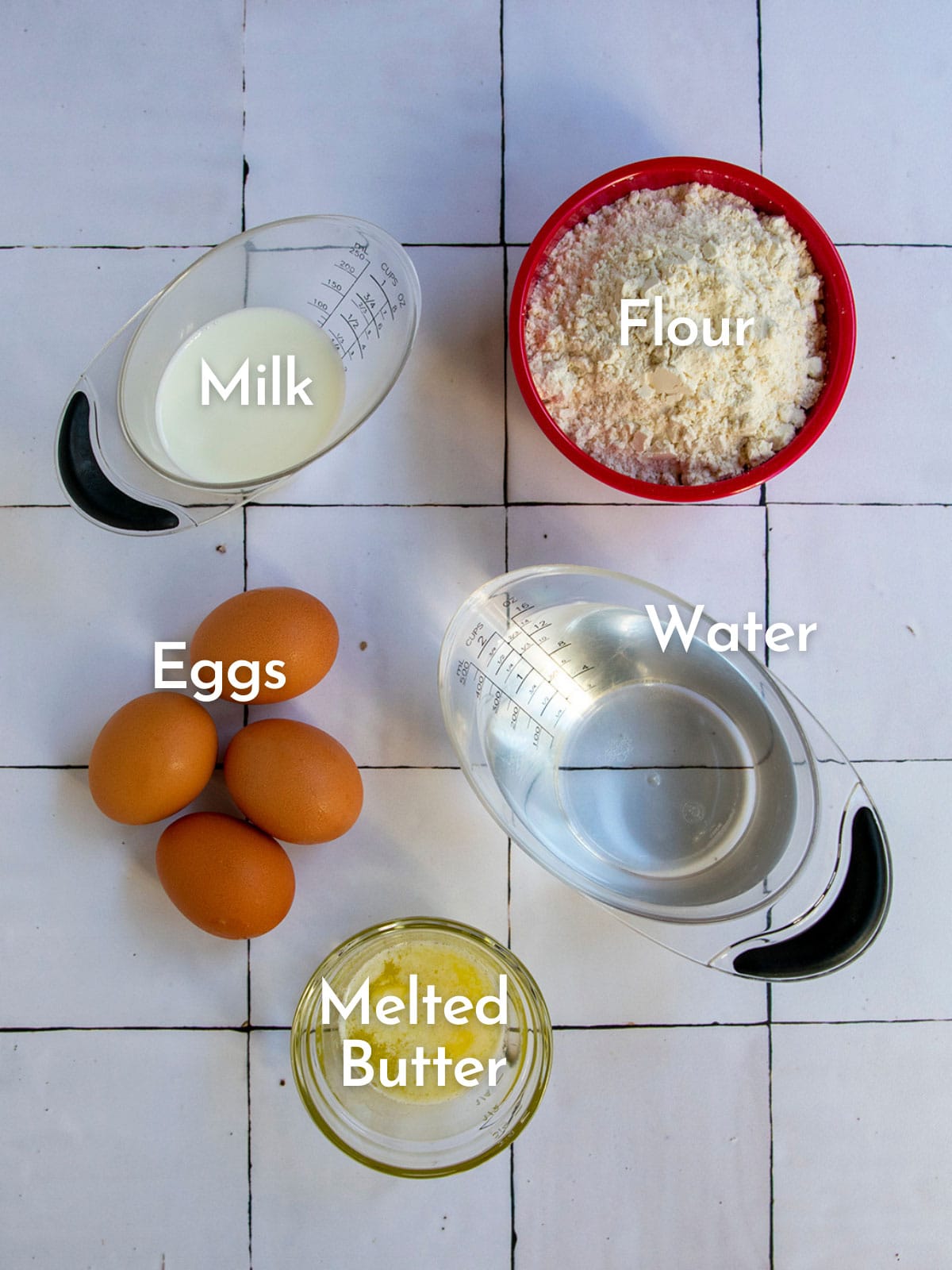Ingredient shot on tile background show eggs, milk, flour, water and melted butter for blintz pancake.