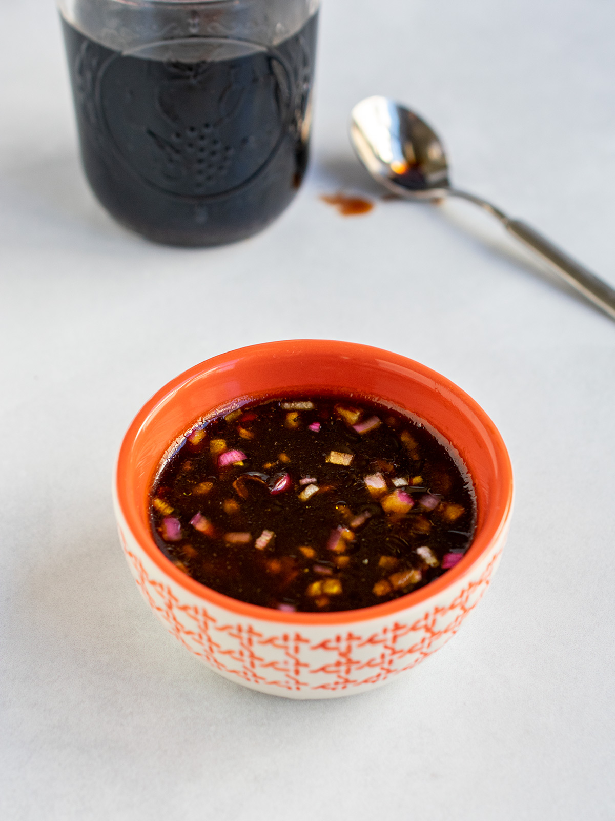 Pomegranate molasses dressing in an orange bowl with a jar of pomegranate molasses in the background with a spoon.