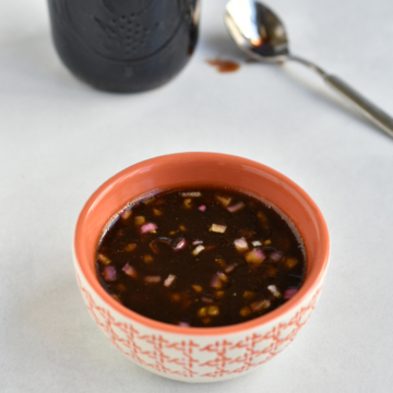 Bowl of pomegranate molasses dressing with a spoon of pomegranate molasses in the background.