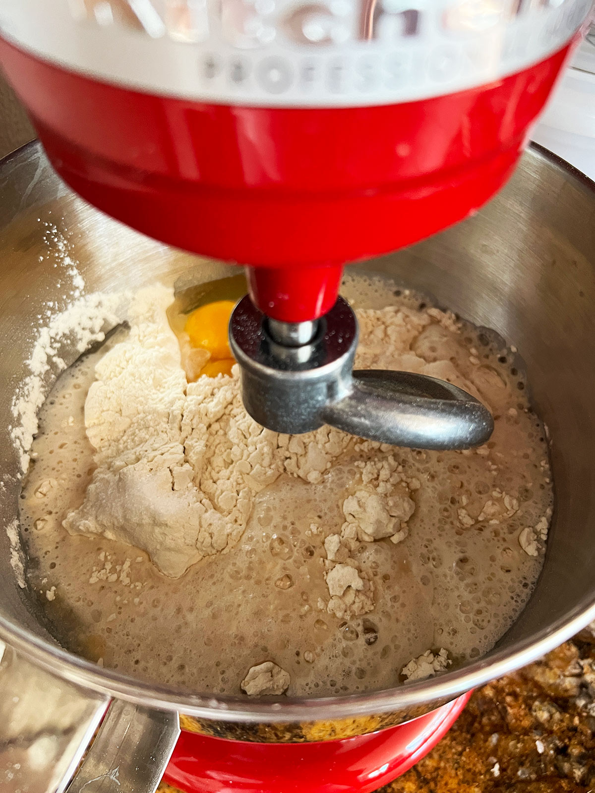 Challah ingredients in the large bowl of a red stand mixer with the dough hook attached.