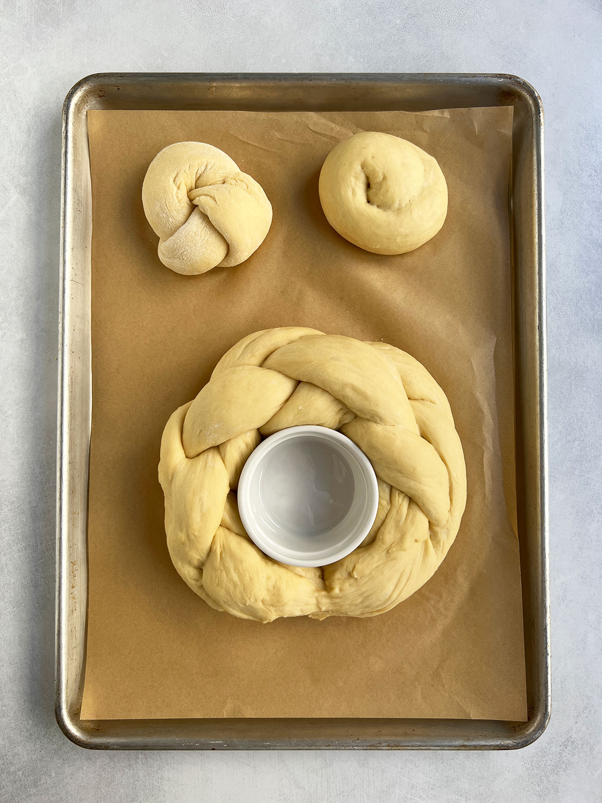 Lonni's challah dough braided and wrapped around a ramekin into a round shape with 2 rolls next to it.