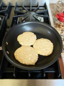 Three pancakes unflipped in a small fry pan on the stove.