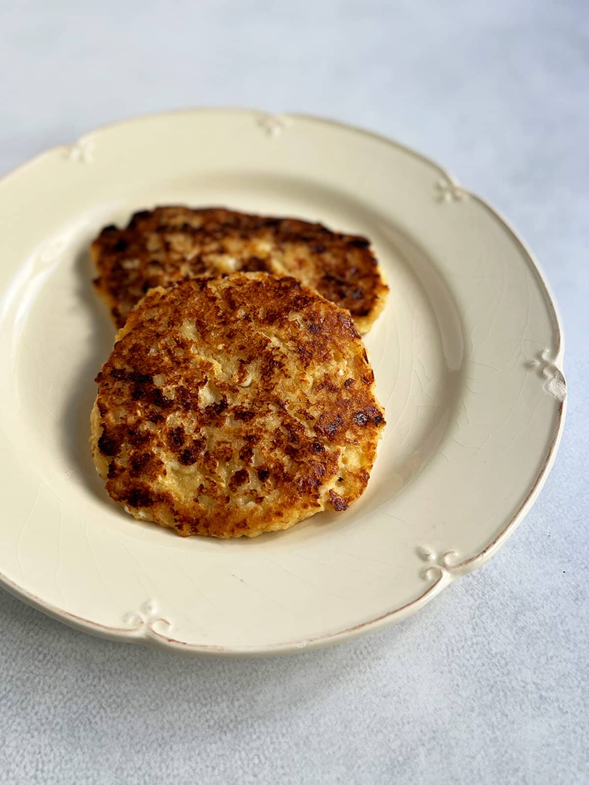 Two cheese latkes on an off white plate with a close up of the top of one of the pancakes.
