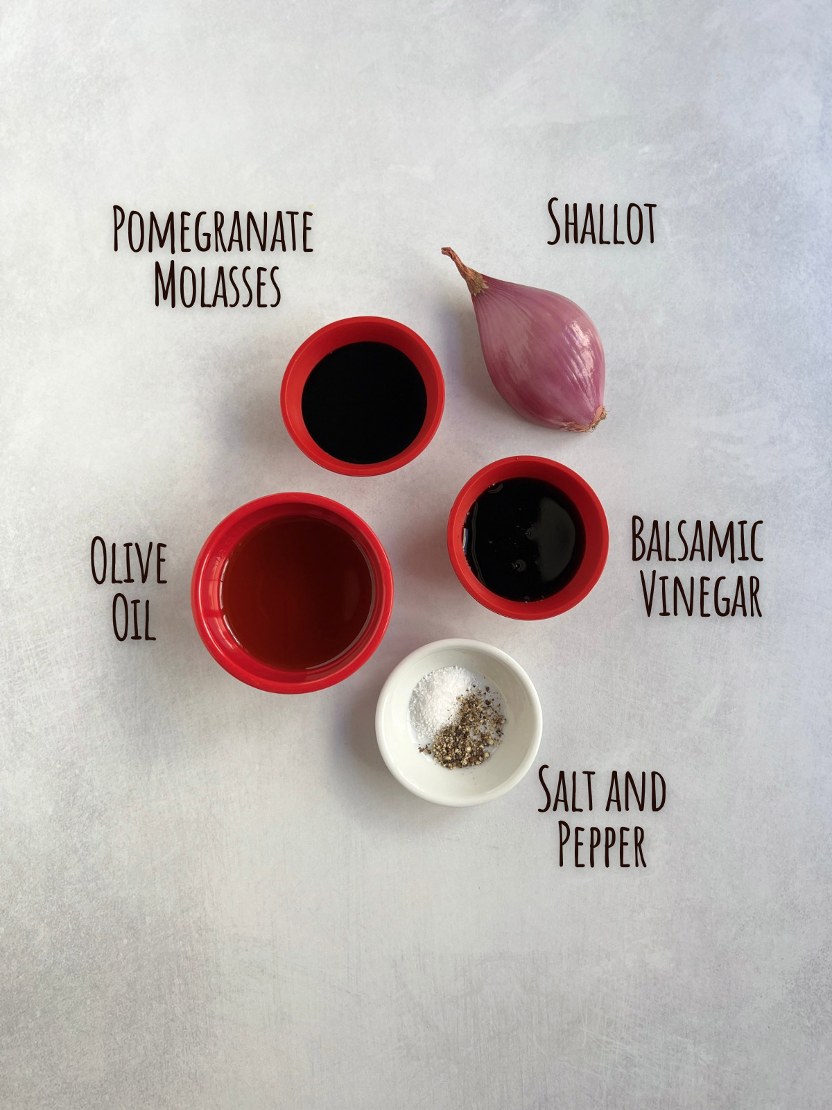 Ingredient shot for pomegranate molasses dressing showing shallot, pomegranate molasses, balsamic vinegar, olive oil and salt and pepper.