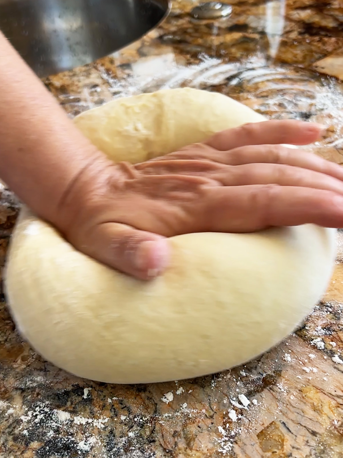 A hand kneading challah dough on a granite counter with flour on it.